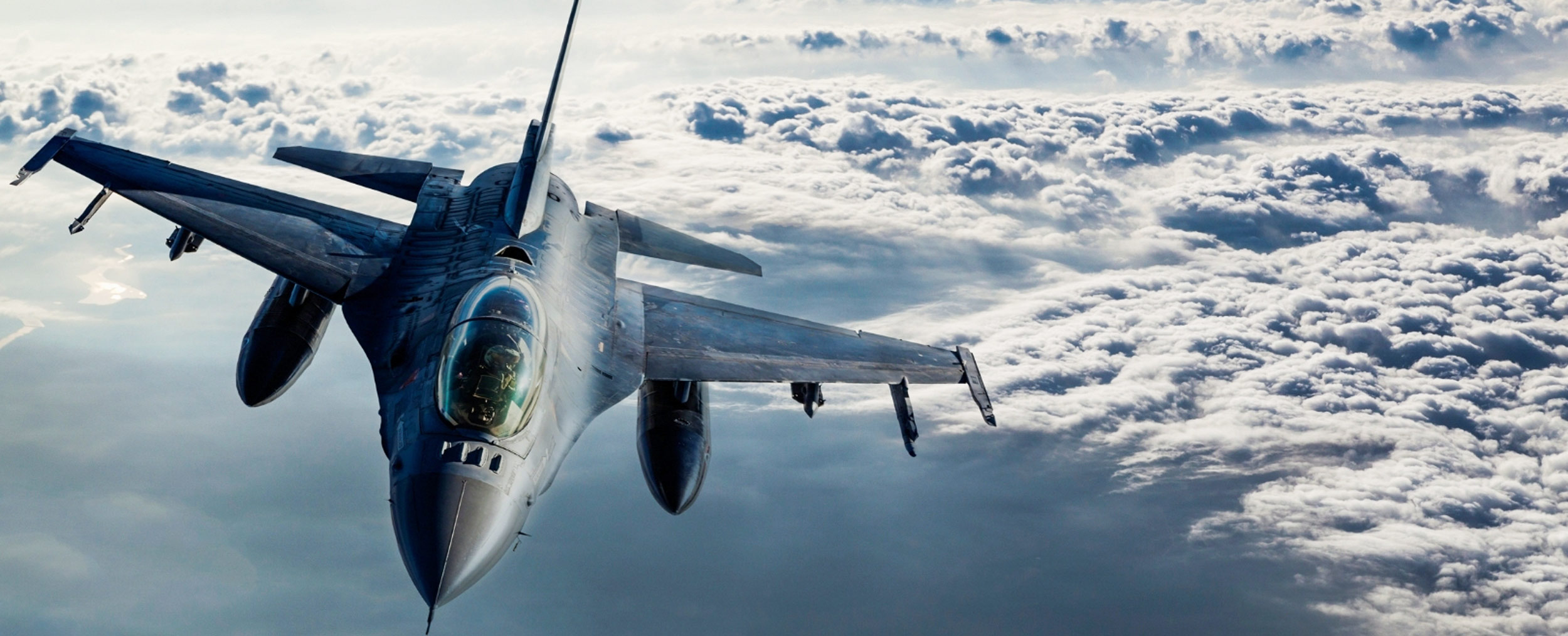 Fighter jet flying above a layer of clouds.