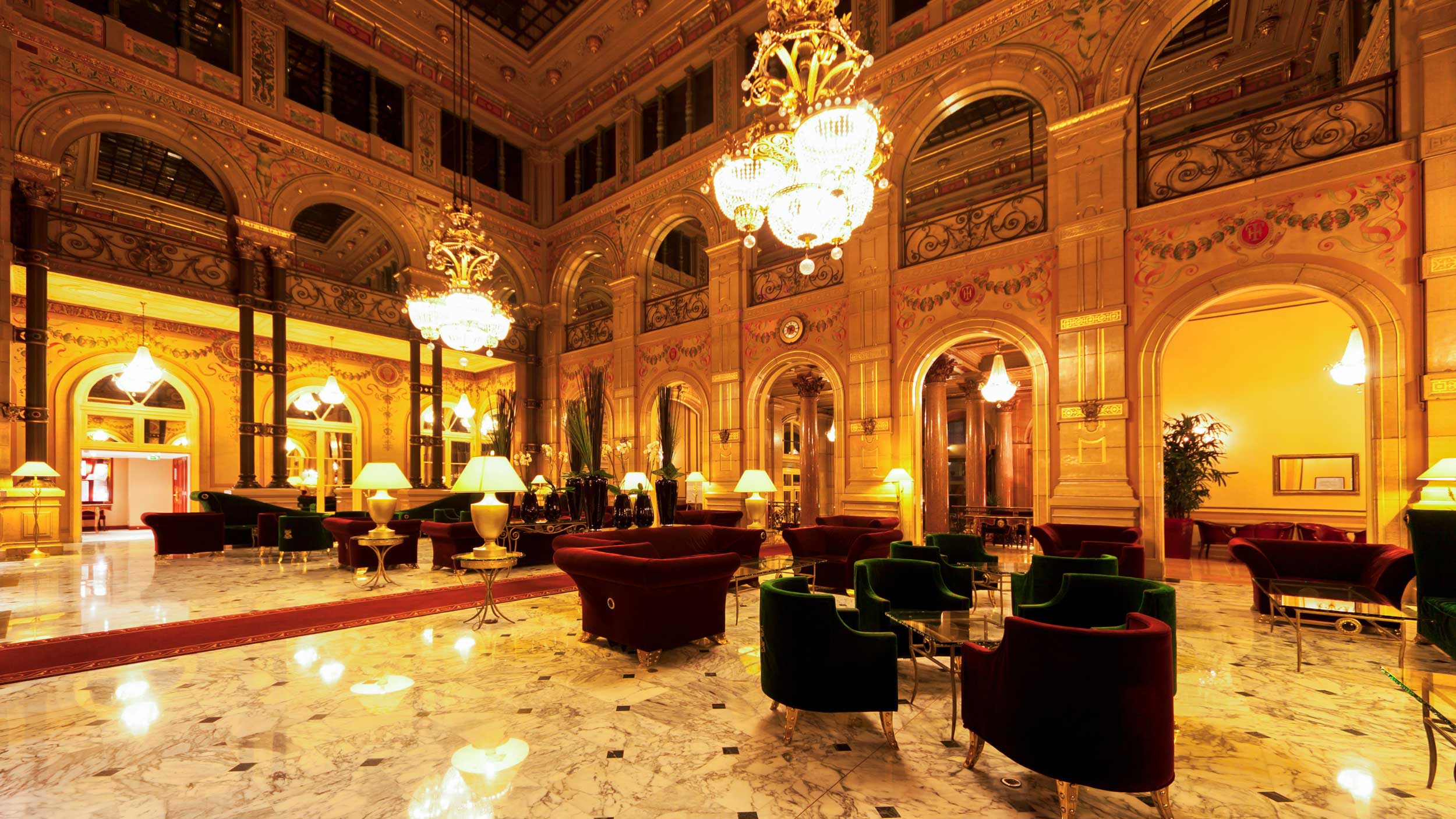 Ornate hotel lobby with chandeliers, marble floors, and lounge seating.